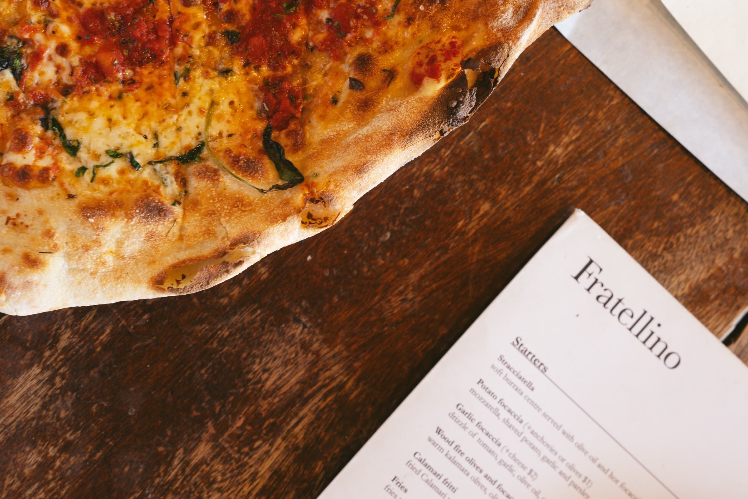 Wood-fired pizza on a timber table beside the Fratellino menu